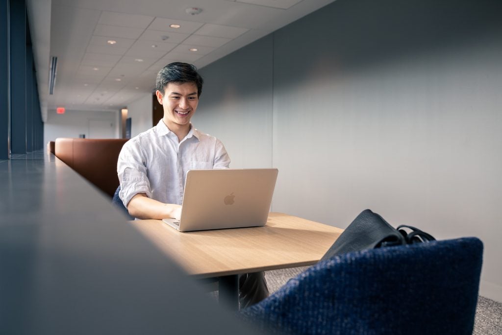 Young Asian man with a laptop at a table while smiling