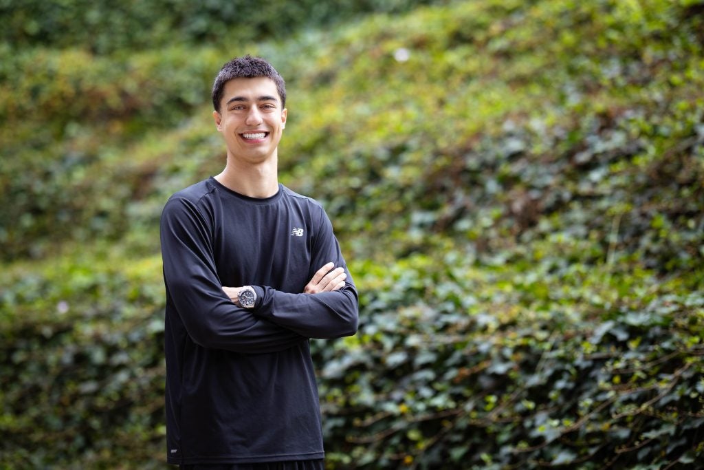 Kiumars in a black shirt with his arms crossed in front of some bushes