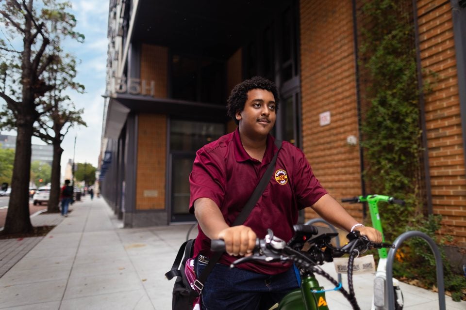 Young Black man riding a bike in a maroon polo shirt
