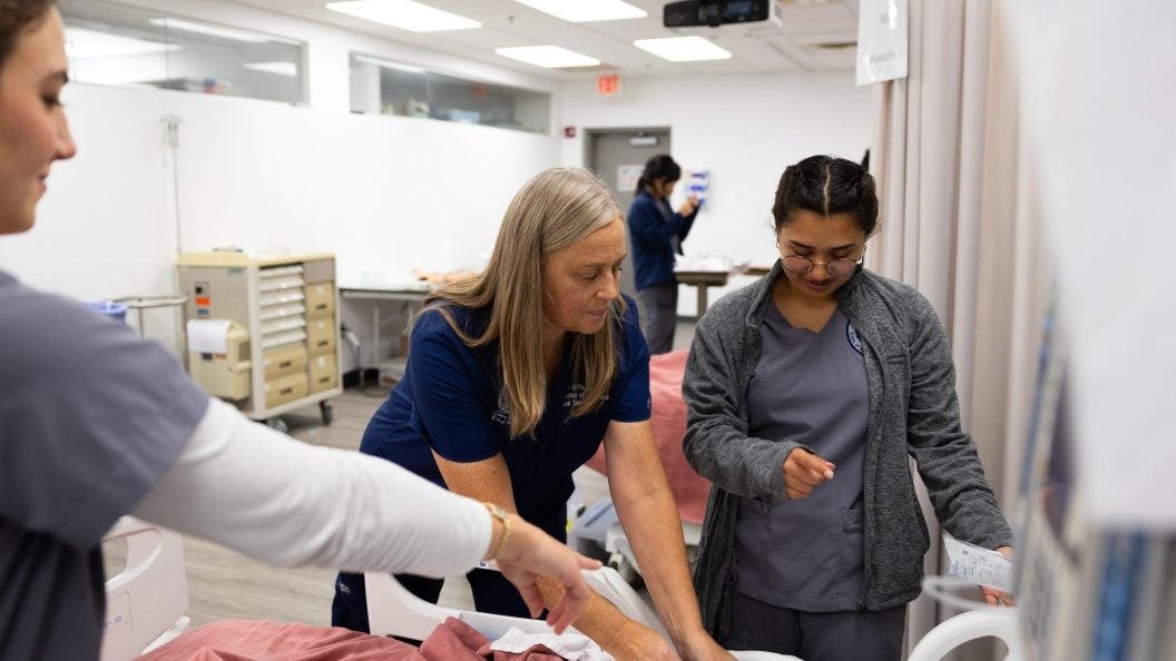 A nurse helps two student nurses assess a mannequin in a simulation