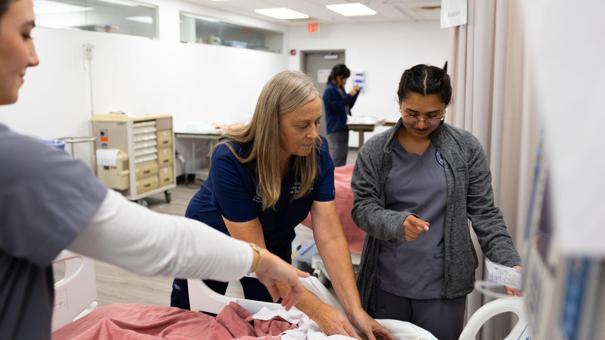 A nurse helps two student nurses assess a mannequin in a simulation