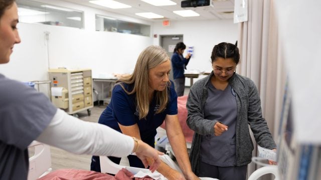 A nurse helps two student nurses assess a mannequin in a simulation
