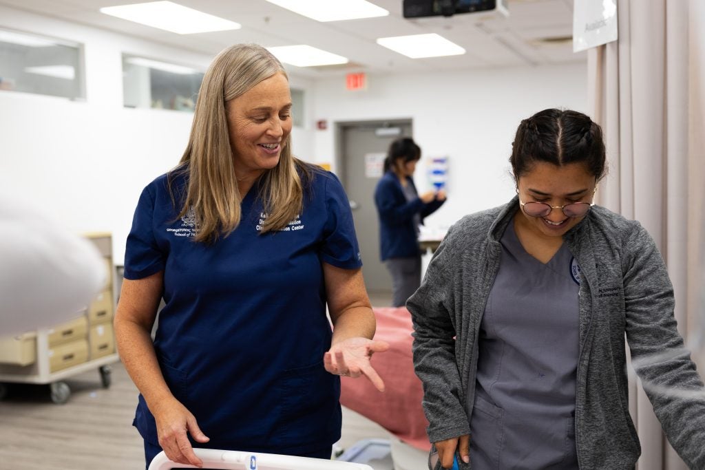 An instructor laughs with a student nursing in a simulated hospital floor