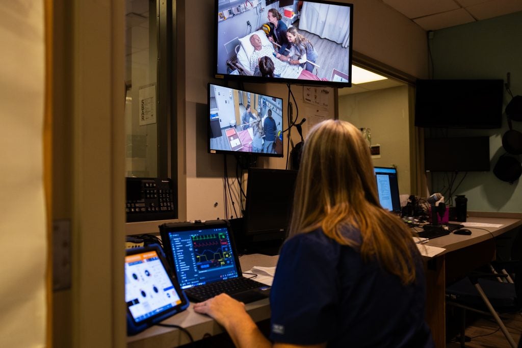 A nurse monitors screens of student nurses working with a patient in a control room