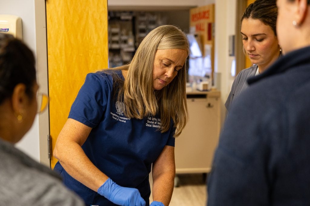 A nurse shows students how to insert an IV into a mannequin's arm
