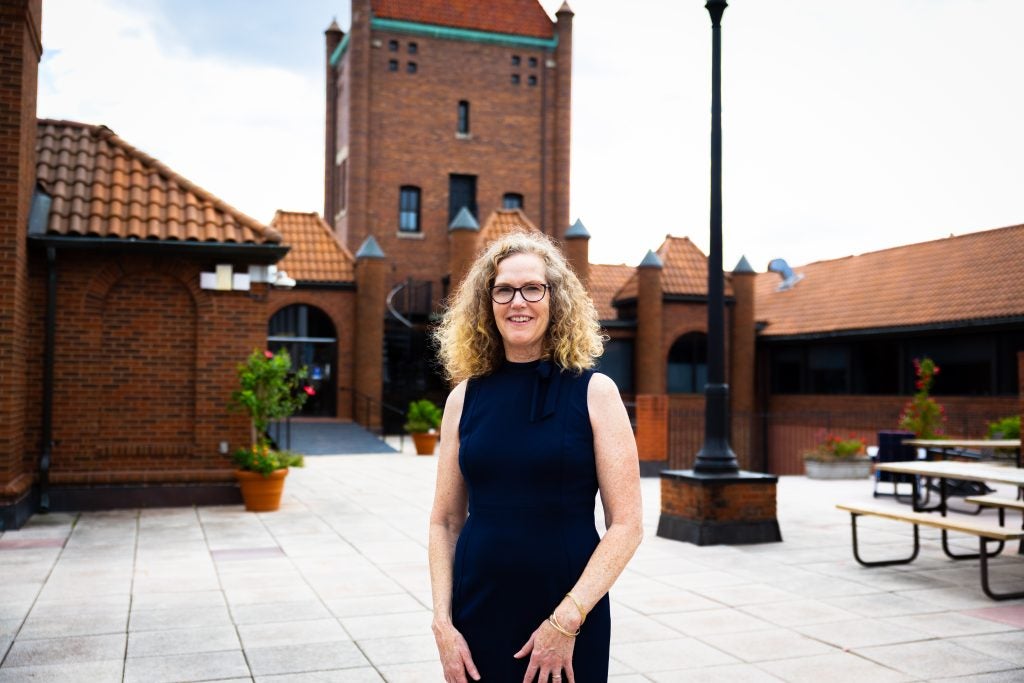 A woman with blonde curly hair in a blue dress smiles on a patio