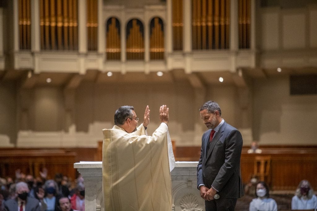 A priest blesses a man wearing a suit on the altar of a church