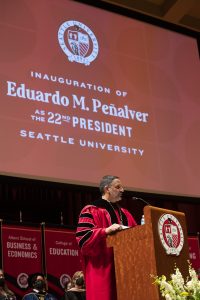 A man in a red academic robe stands behind a podium at Seattle University