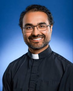 A Jesuit in a clerical collar smiles