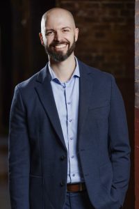 Caucasian man with a beard smiling while wearing a blue blazer