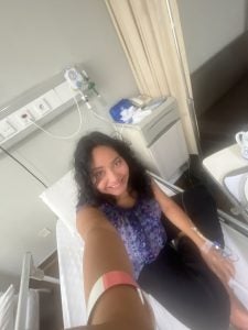 A young woman on a hospital bed smiling for a selfie