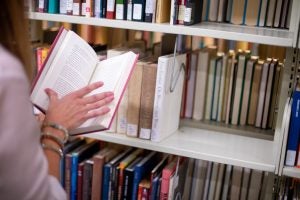 Woman opens a book by a bookshelf