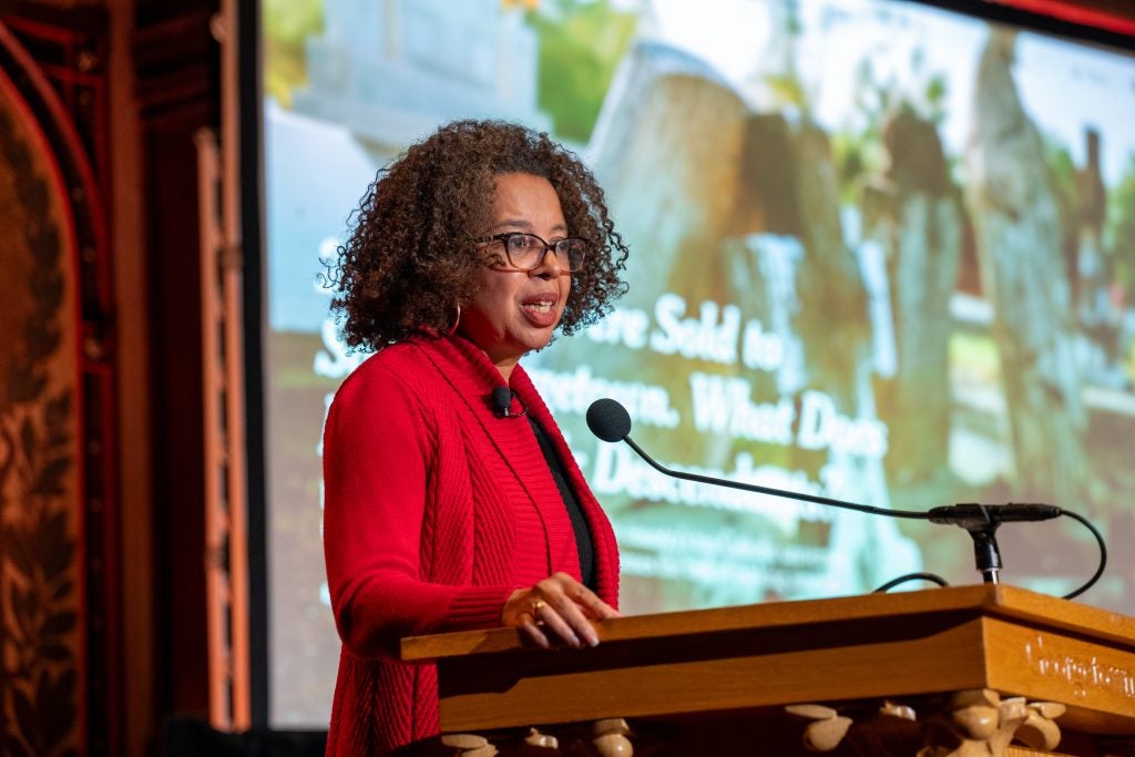 Black woman in red jacket at a podium in Gaston