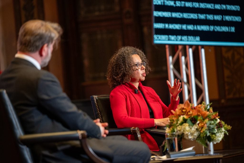 A Black woman in a red jacket on stage on Gaston