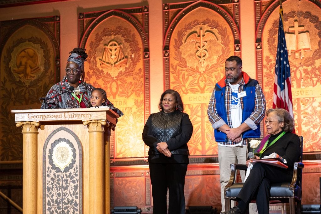 Five Black men and women and a child on stage in Gaston Hall