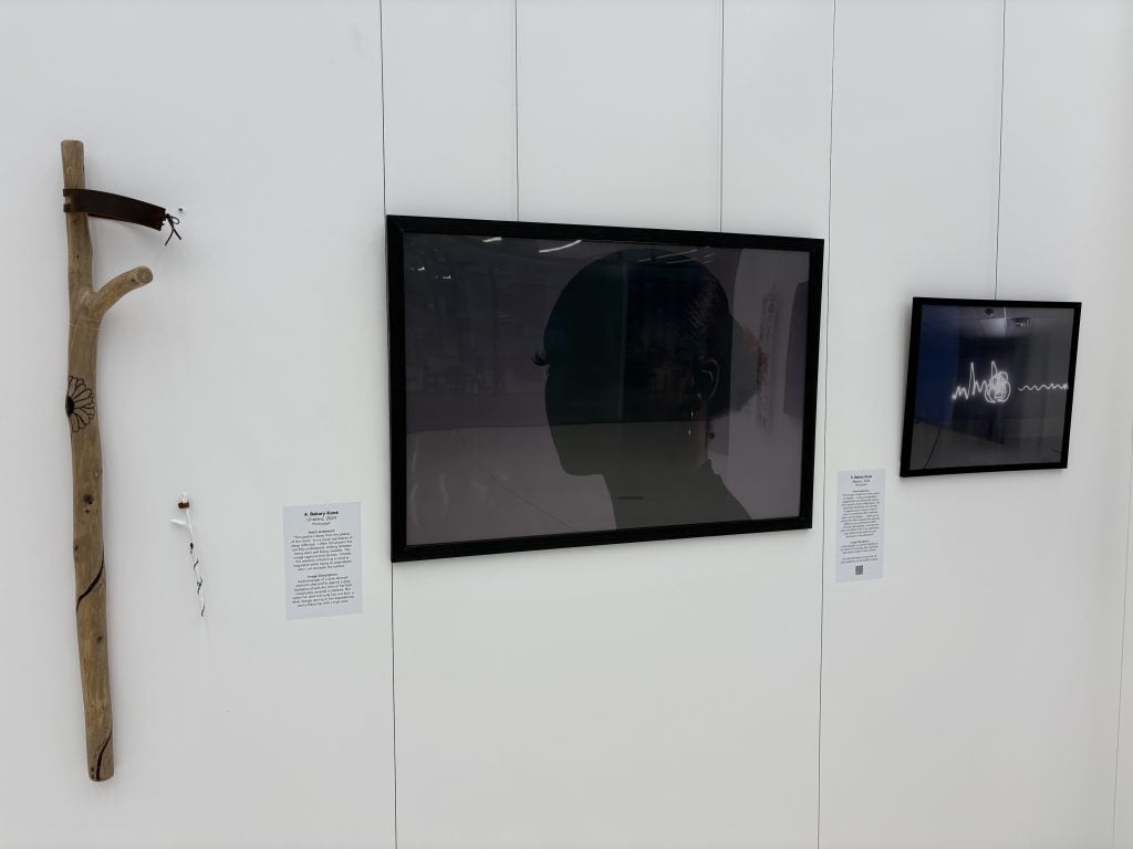 A photograph of a woman hands in an exhibit next to a mobility device and another photograph