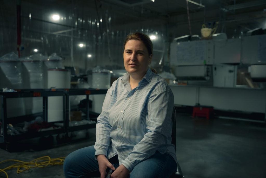 A woman in a blue button-down sits in a chair during the filming of a documentary