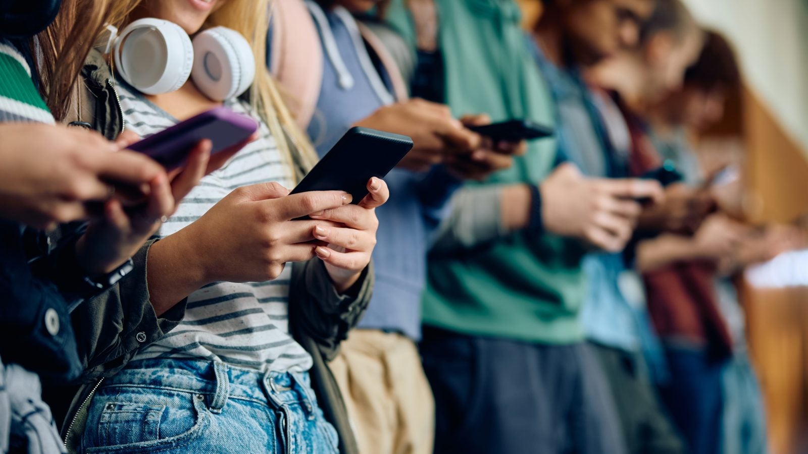 Close up of teenage girl and her friends using mobile phones at high school hallway.