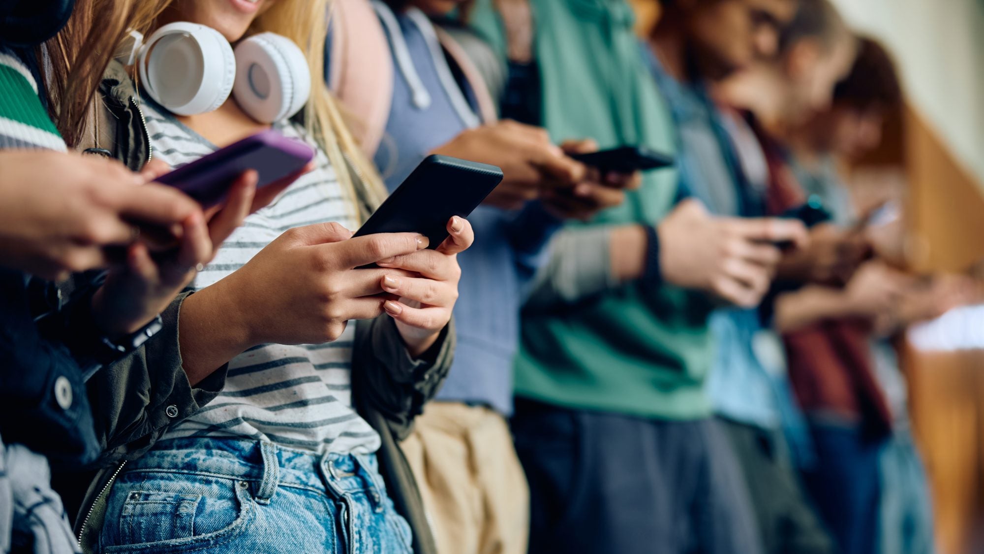 Close up of teenage girl and her friends using mobile phones at high school hallway.