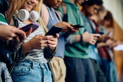 Close up of teenage girl and her friends using mobile phones at high school hallway.