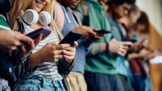 Close up of teenage girl and her friends using mobile phones at high school hallway.