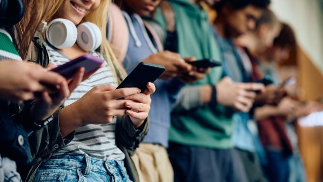 Close up of teenage girl and her friends using mobile phones at high school hallway.