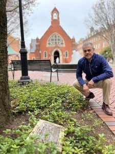 A man poses with a plaque in a courtyard outside a chapel