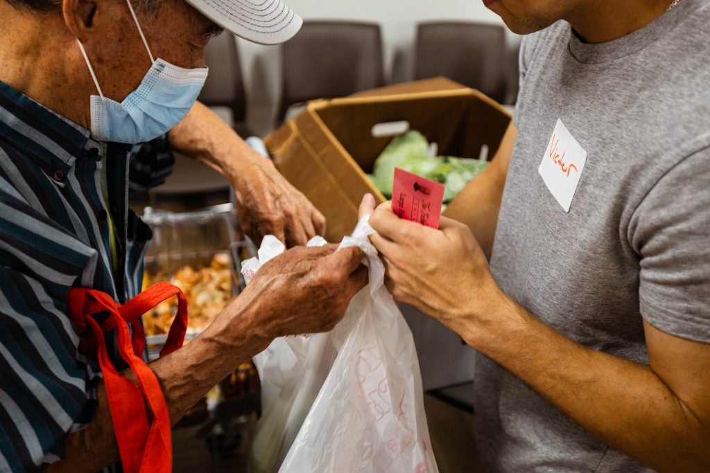 A student helps a client of a food pantry who's wearing a mask with his bag of groceries
