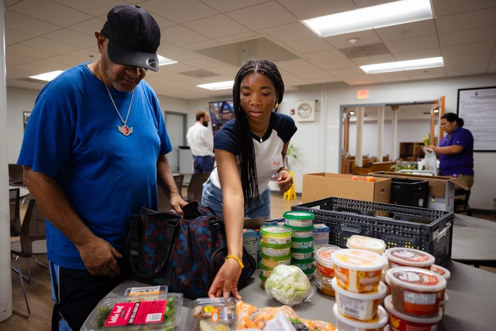 A student helps a client of a food pantry load his bag with groceries
