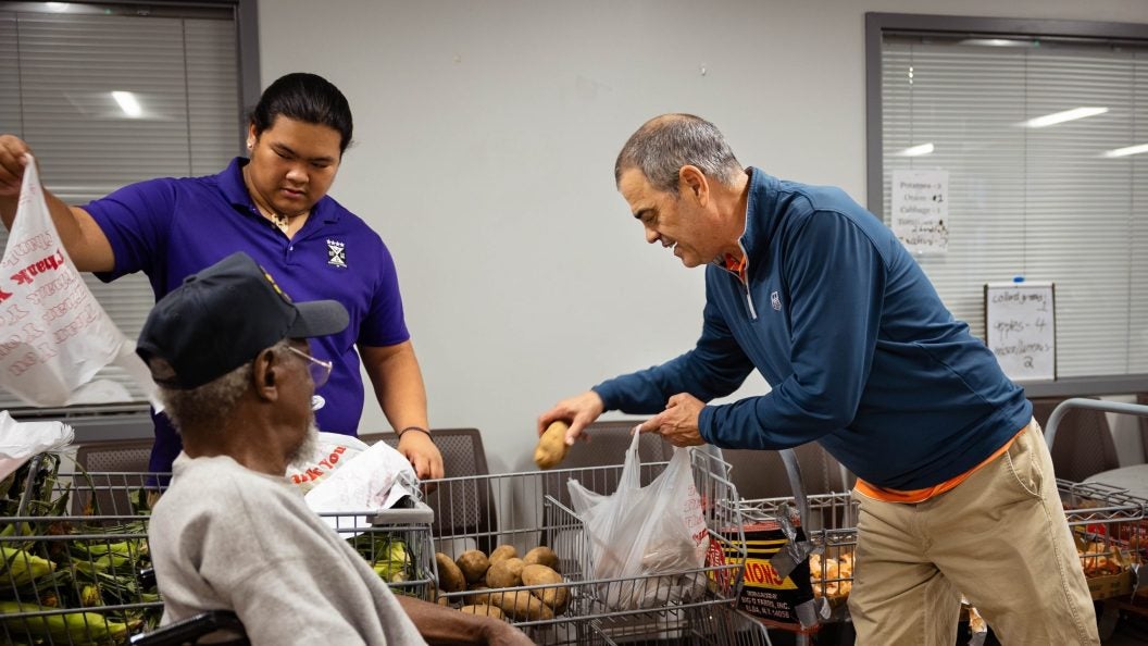 Two men help a man in a wheelchair with groceries