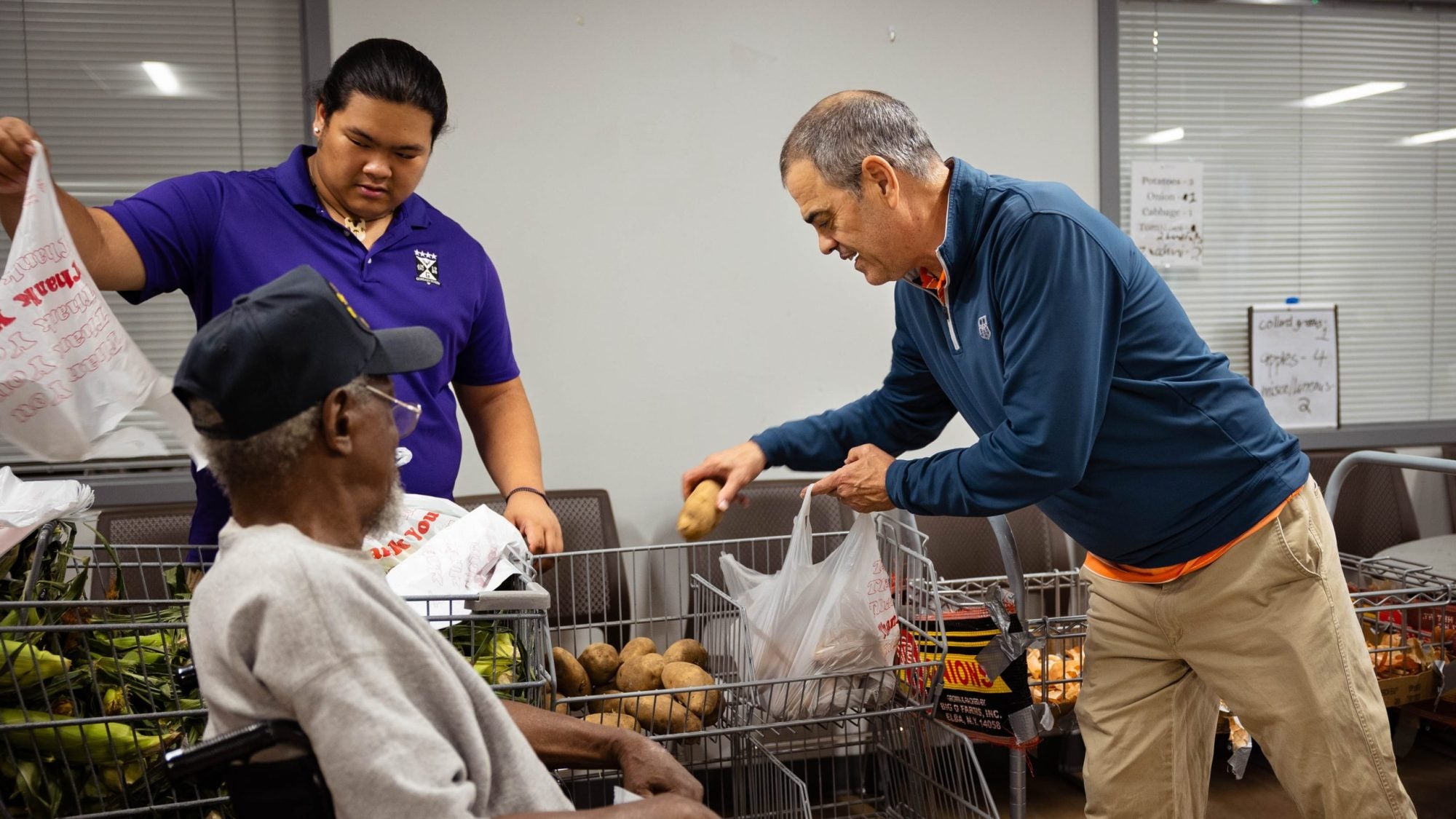 Two men help a man in a wheelchair with groceries