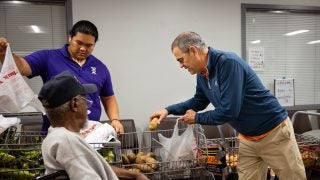 Two men help a man in a wheelchair with groceries