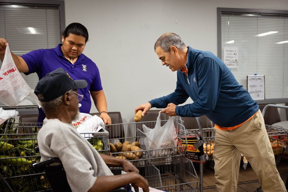 Two men help a man in a wheelchair with groceries