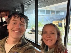 A young man and woman at the zoo looking at a panda