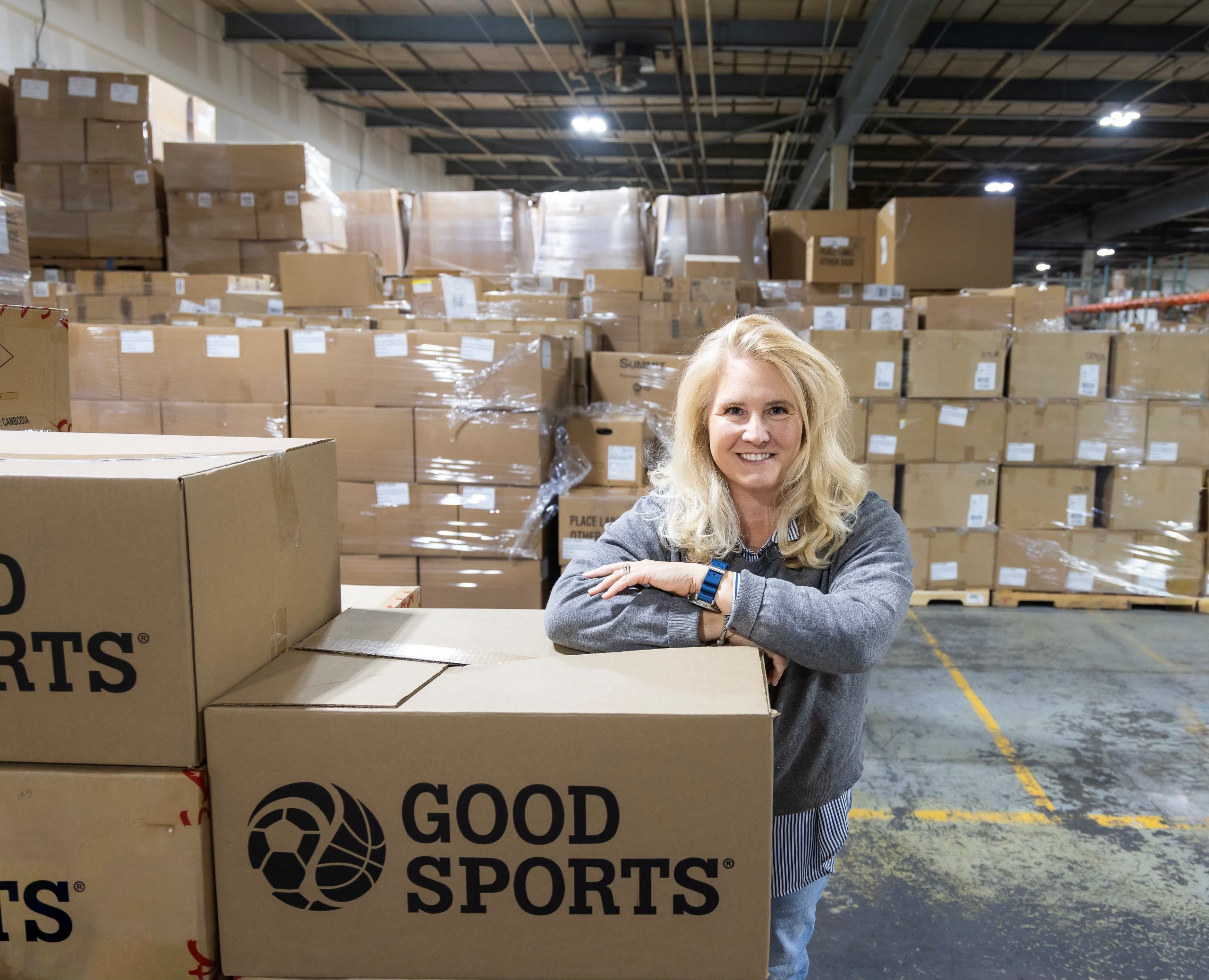 A blonde woman with some Good Sports boxes in a warehouse