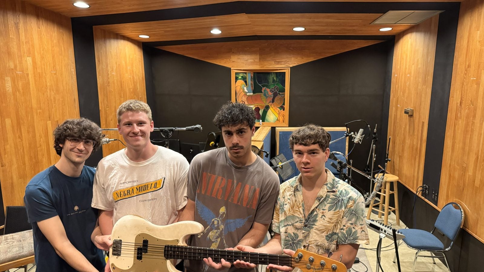 Four young men hold a guitar in a studio