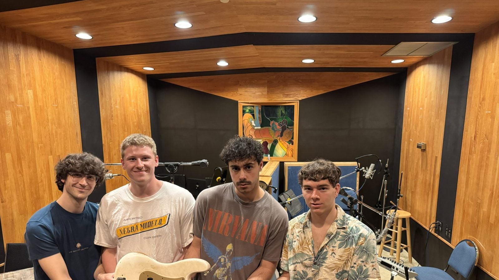 Four young men hold a guitar in a studio