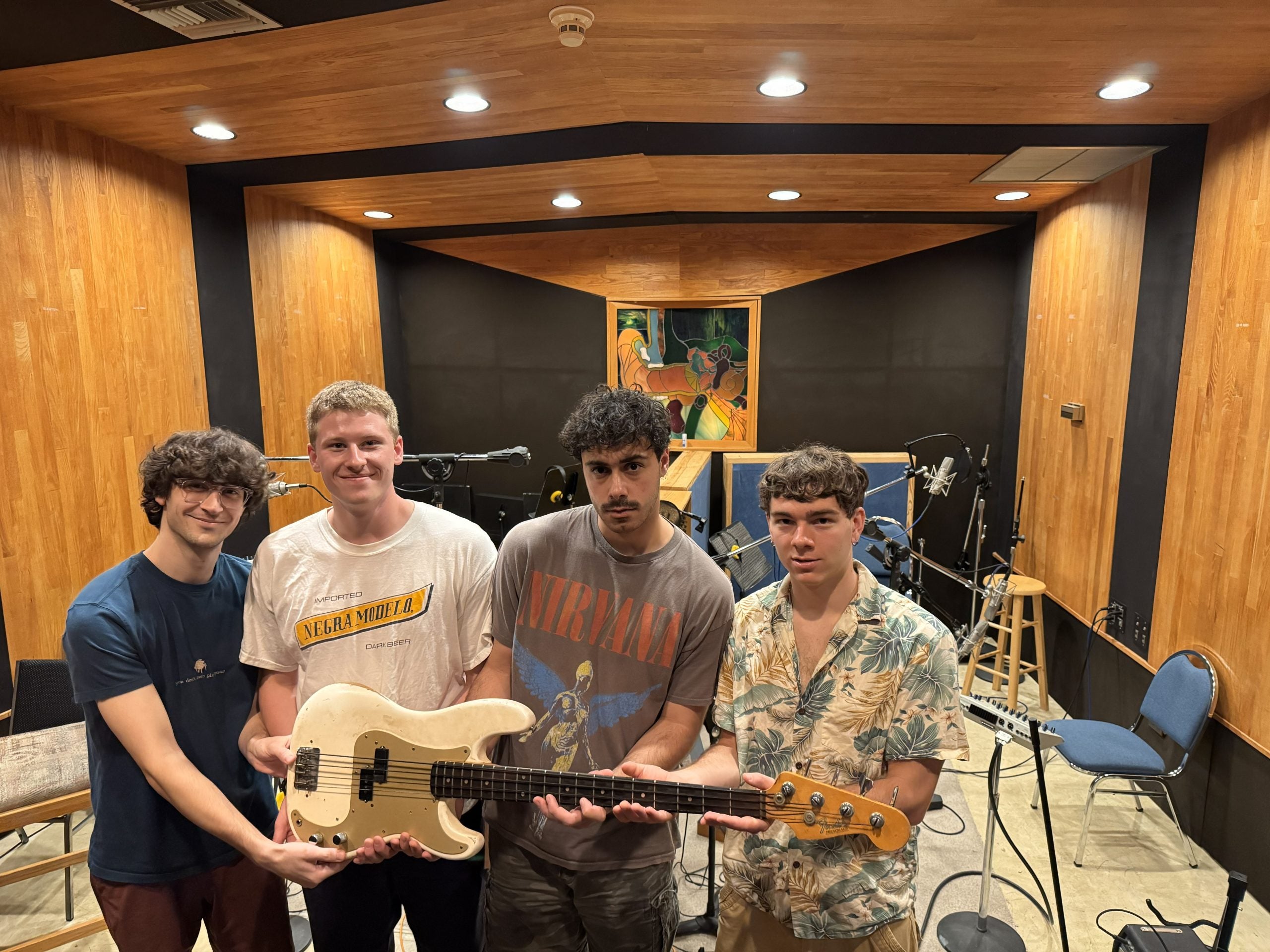 Four young men hold a guitar in a studio