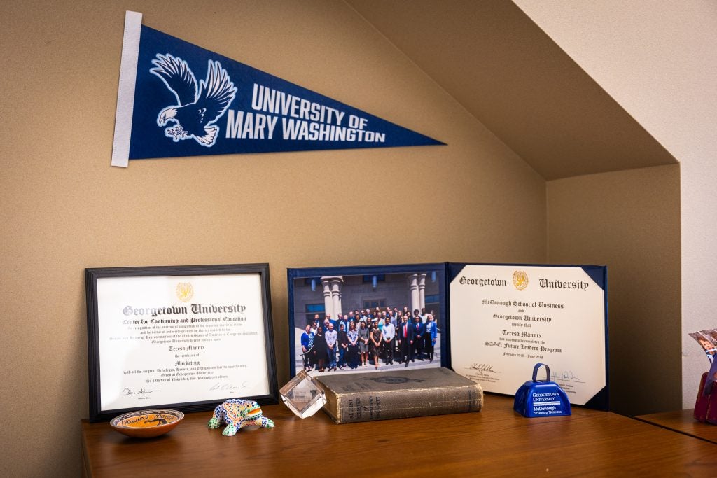Two university degrees are propped up on a desk next to a photo. Above is a flag that says "University of Mary Washington"