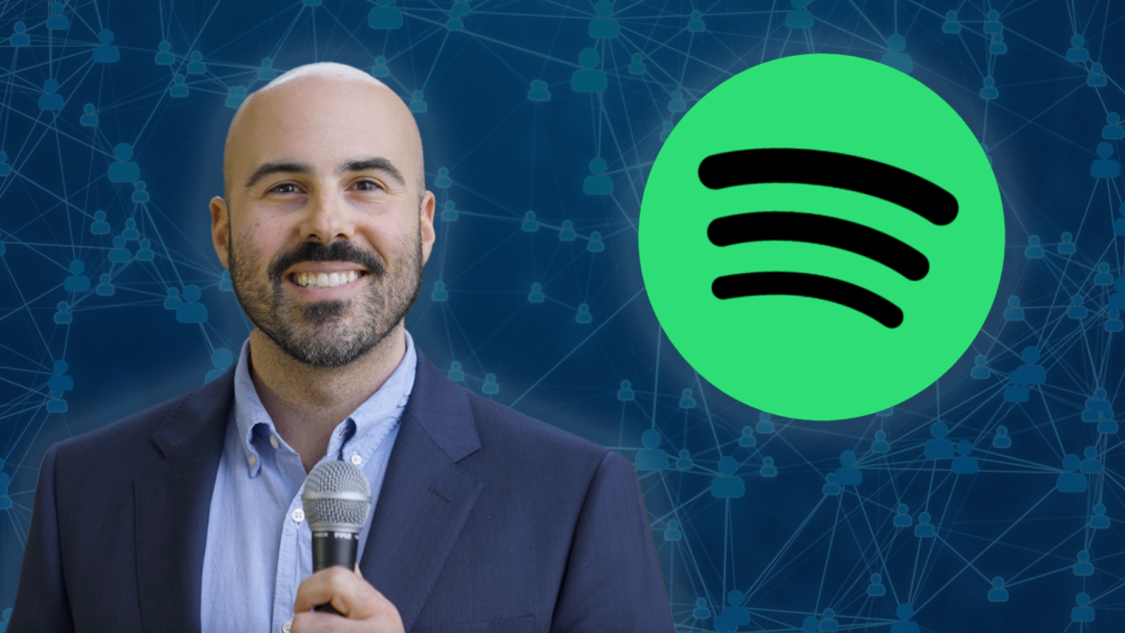 A man in a suit holds a microphone. Behind him is Spotify&#039;s green logo with three curved lines