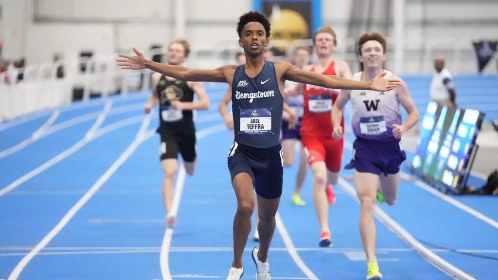 A young Black man celebrates after crossing a finish line at a race