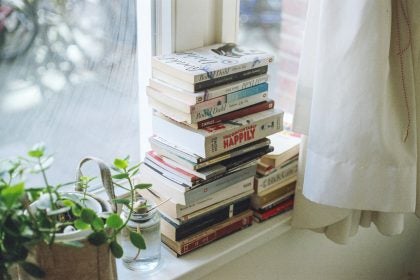 A stack of books on a windowsill next to a plant