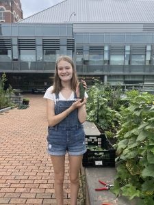 Young white woman holds up a vegetable in a garden