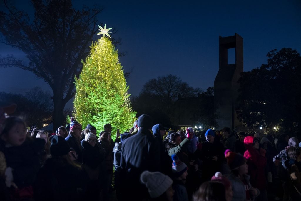 a crowd of people stand around a yellow and green christmas tree