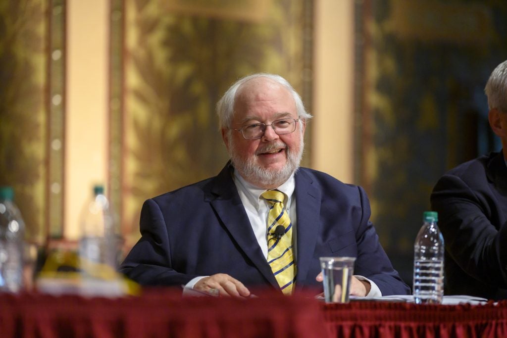 A man in a blue suit and tie smiles behind a panel.