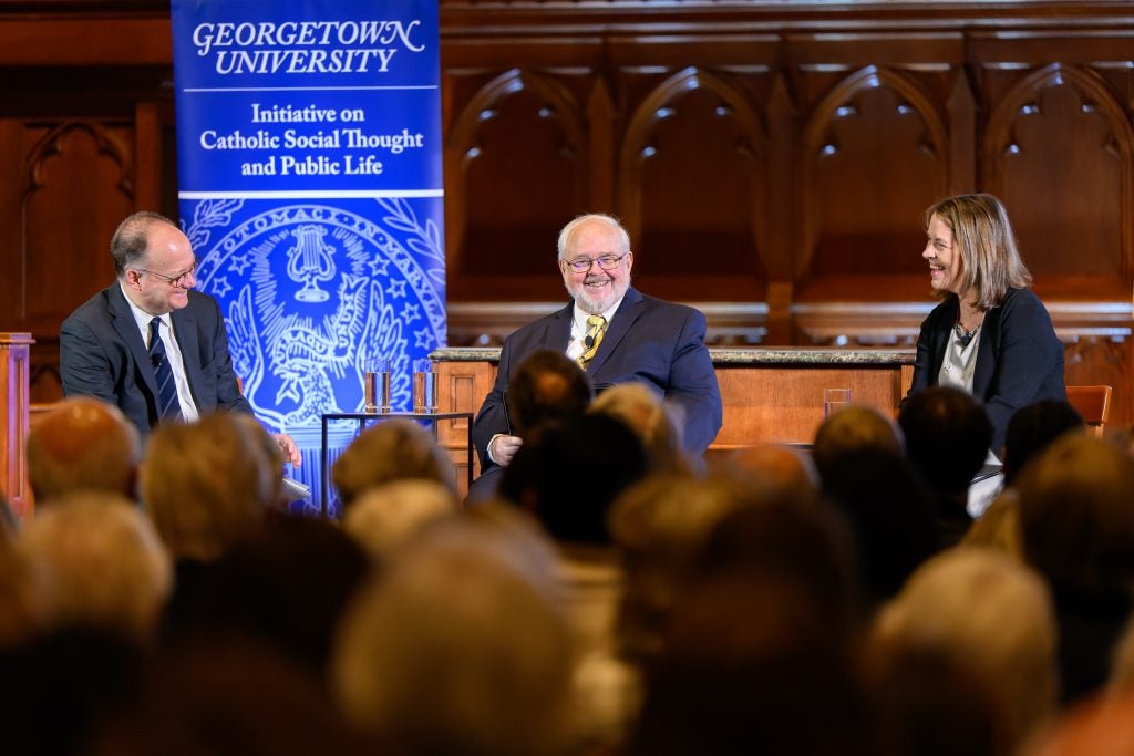 Three people sit on a panel in front of a crowd and talk