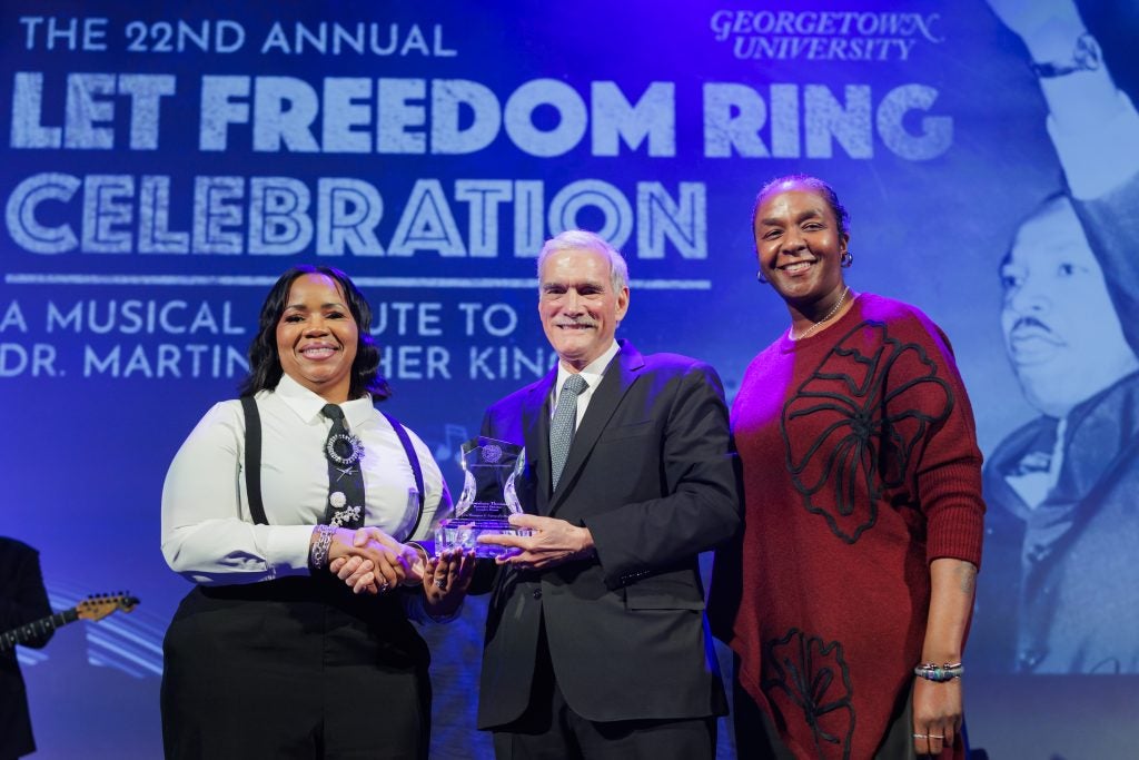 A Caucasian male with two Black woman on stage presenting an award