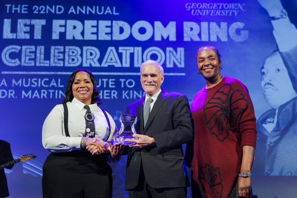 A Caucasian male with two Black woman on stage presenting an award