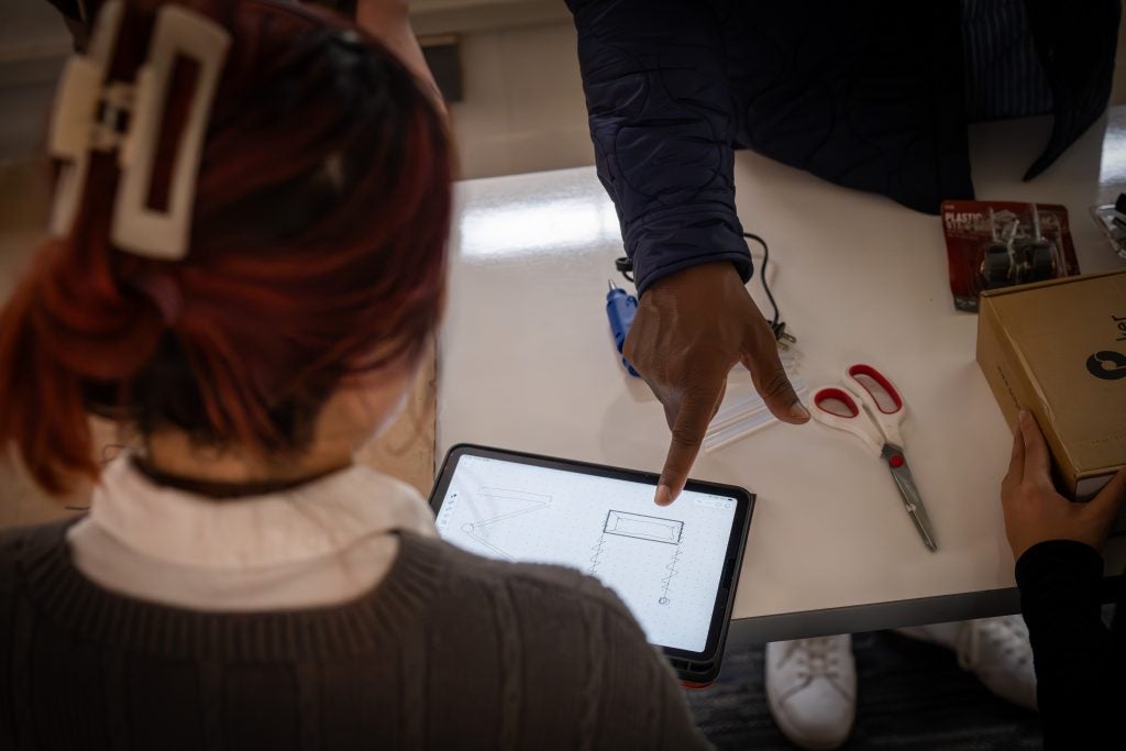 A student looks at an iPad with a sketch on it while another student points to it.