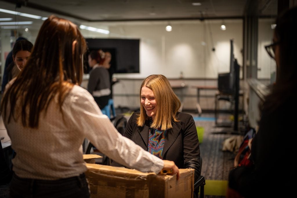 A student presents a cardboard cut-out of a podium to another woman who smiles